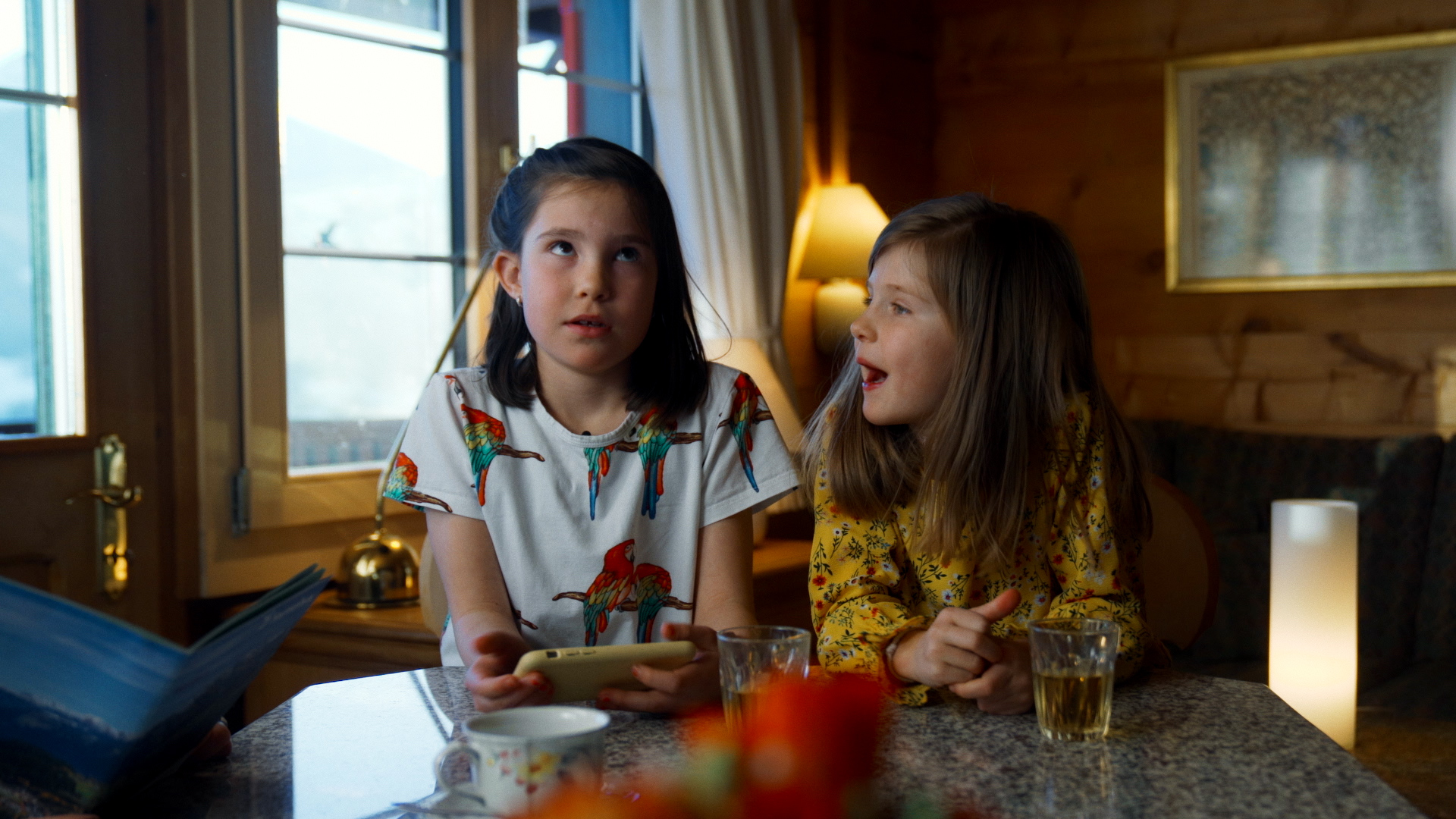 Two children in a Swiss mountain chalet sitting next to each other with an annoyed look. 